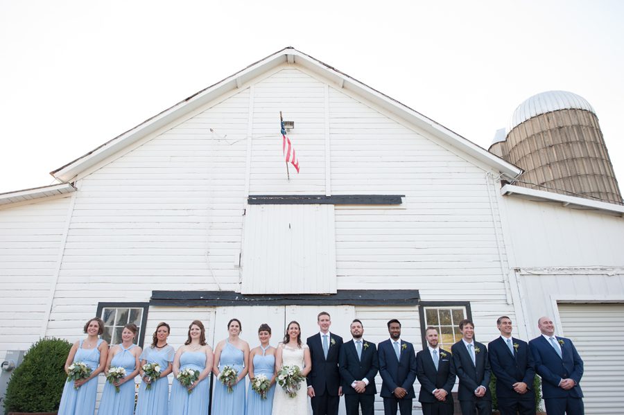 wedding party photo in front of the barn with an american flag